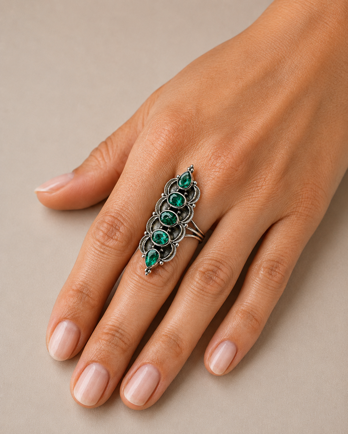 Sterling silver five-stone emerald ring worn on hand, oval green stones in bezel settings