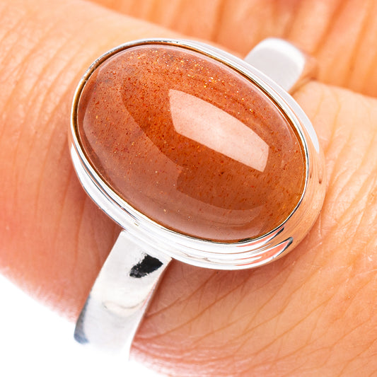 Sterling silver ring with oval orange sunstone cabochon, close-up on finger
