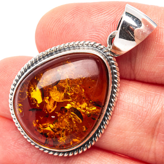 Oval amber stone pendant in textured sterling silver frame, shown on hand