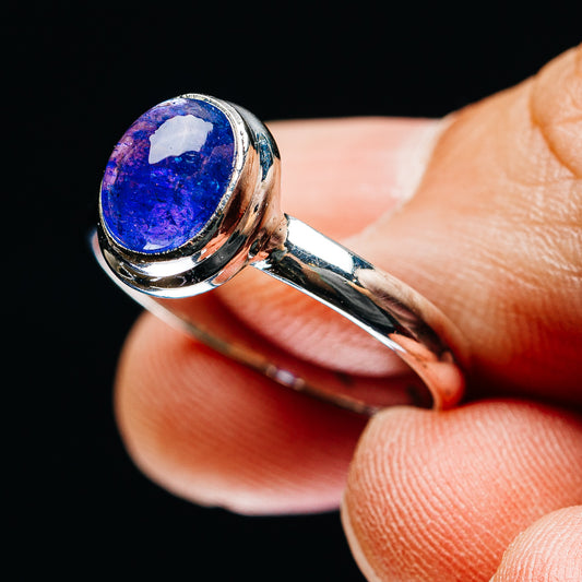 Oval blue-purple gemstone ring with silver band, side view on fingertip