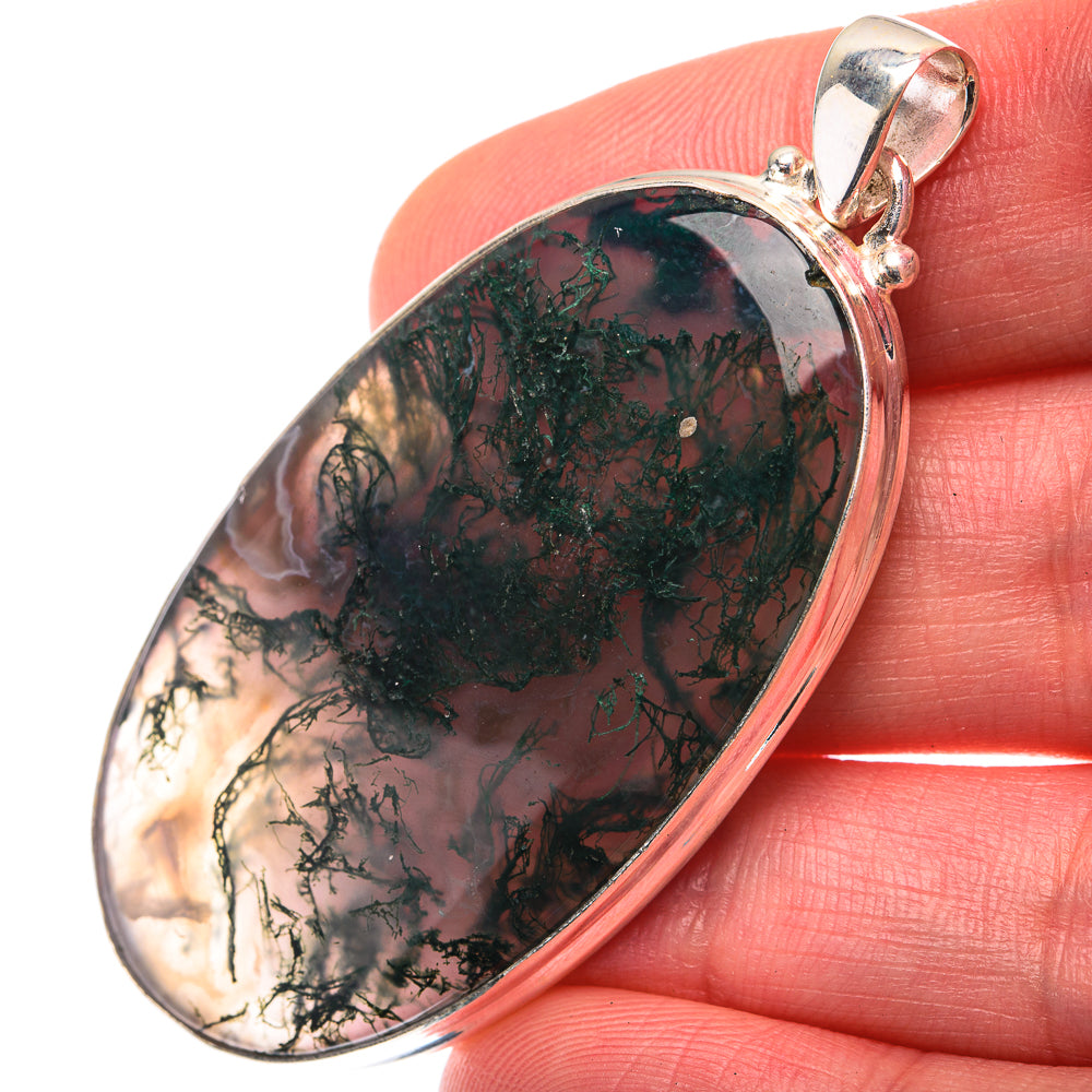 Oval green moss agate pendant with silver bezel and bail, on finger.