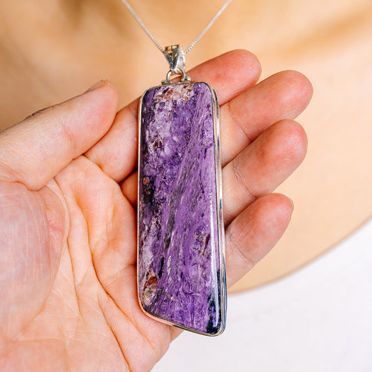 Purple charoite pendant with sterling silver frame, held in an open palm