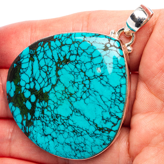Large turquoise cabochon pendant, silver bail visible on hand