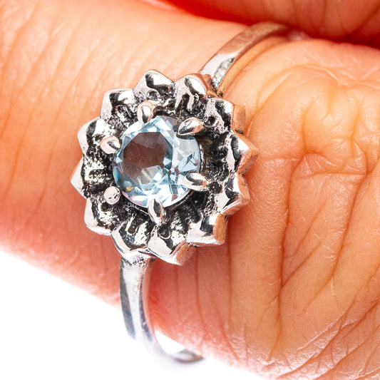 Sterling silver blue topaz ring with ornate halo setting, close-up on finger