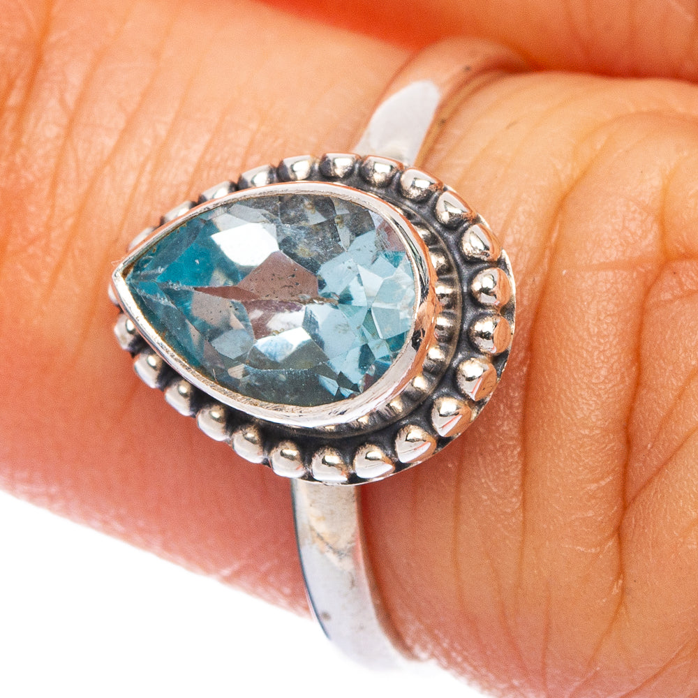 Blue topaz oval gemstone ring in silver with bead-edge halo on finger