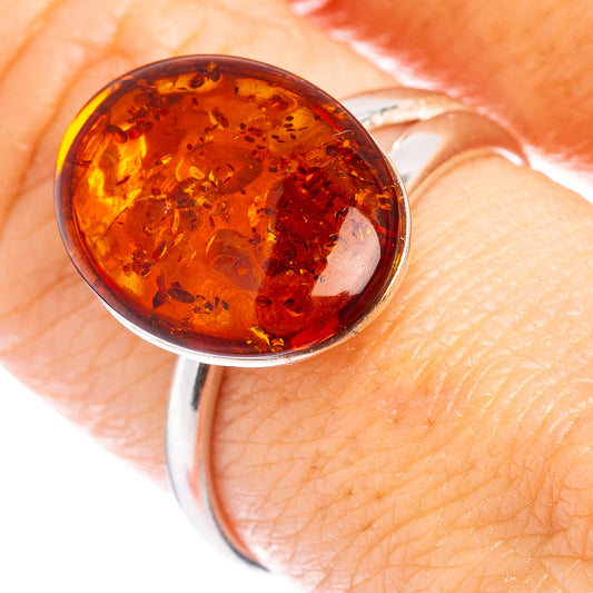 Dark orange amber cabochon ring with silver bezel, close-up on finger