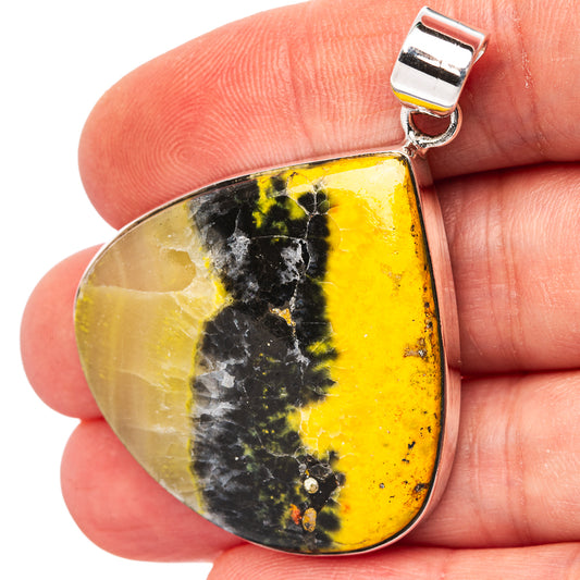 Yellow and black jasper teardrop pendant with silver bail, held for scale
