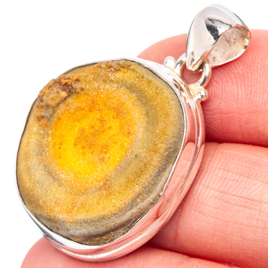 Oval amber-gold jasper pendant on sterling silver bail, held against finger.
