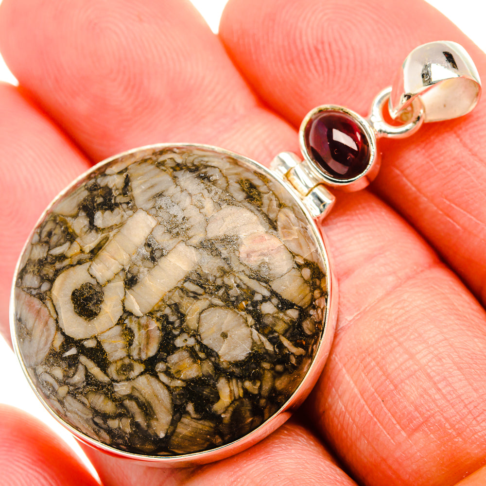 Round fossil stone pendant in silver bezel with red garnet accent
