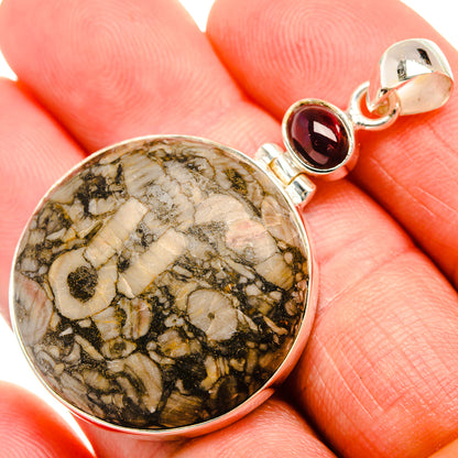 Round fossil stone pendant in silver bezel with red garnet accent