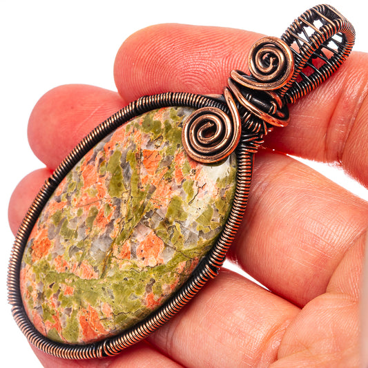 Unakite teardrop pendant close-up: mottled green-orange stone in copper spiral bezel