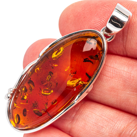 Amber oval pendant with silver frame and bail, held on fingertips