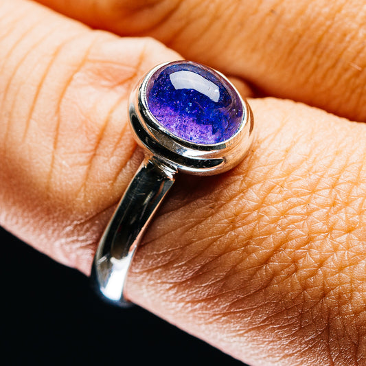 Tanzanite-style oval ring with blue-purple gemstone in silver bezel, worn on finger