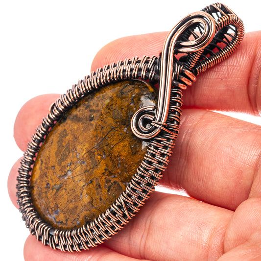 Oxidized copper wire-wrap pendant held in hand, oval agate stone and loop bail