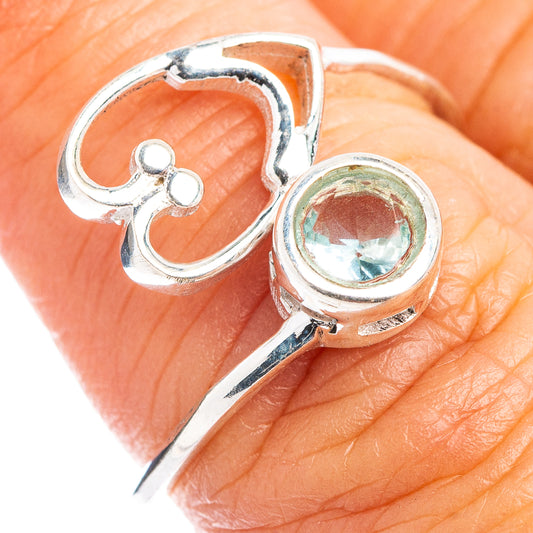 Dainty sterling silver ring with open heart bezel and blue round gemstone on finger