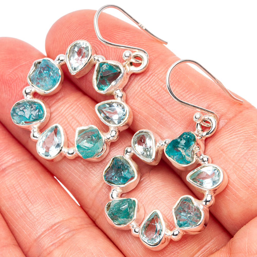 Sterling silver hoop earrings with blue-green gemstones on an open palm