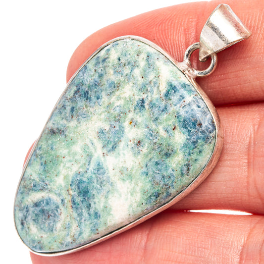 Blue-green kyanite cabochon teardrop pendant with silver bail, shown on fingertip.