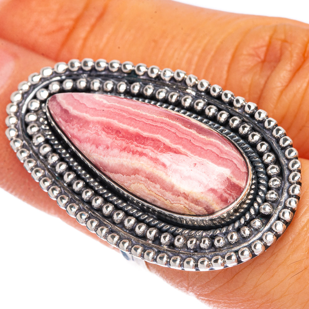 Teardrop rhodochrosite set in silver ring with black trim and bead border, close-up.