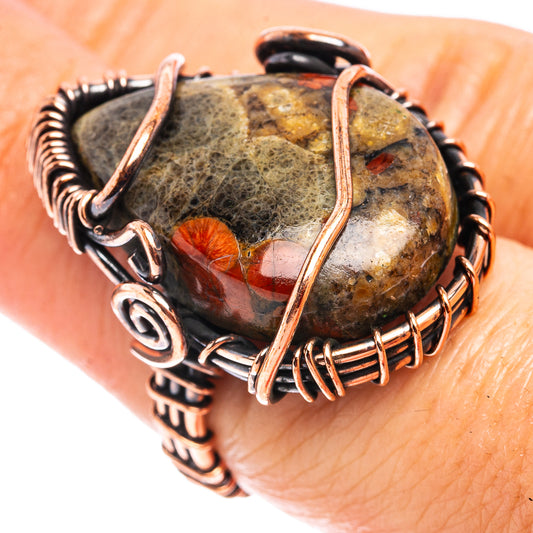 Oxidized copper wire wrap ring with dark oblong stone and red patch, on finger