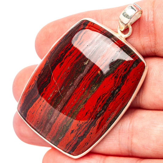 Rectangular red jasper pendant with silver edge and loop bail, held in hand