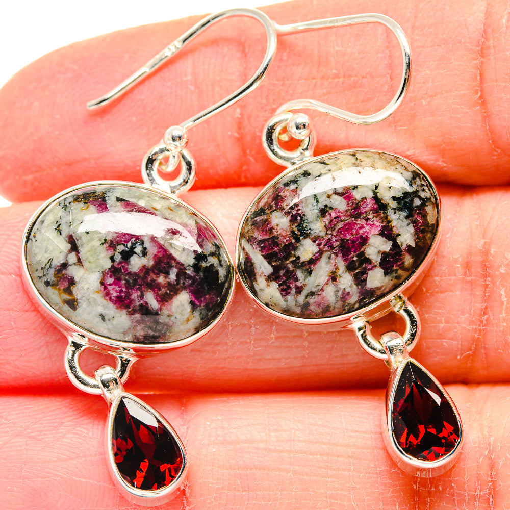 Oval eudialyte and red garnet drop sterling silver earrings on fingertips, close-up