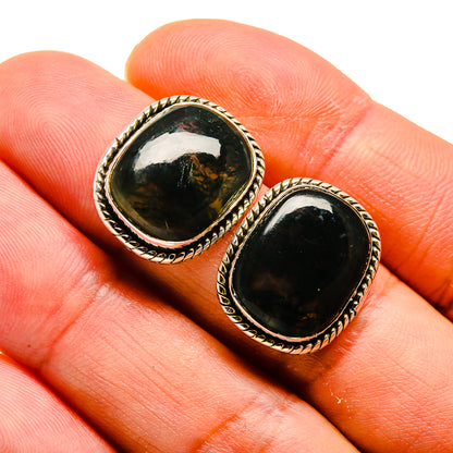 Oval green moss agate stud earrings in silver-toned bezel, close-up on fingertips