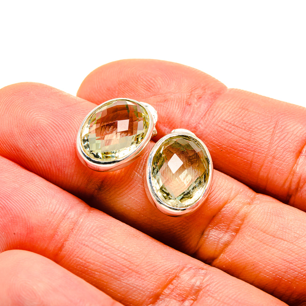 Close-up of oval faceted green amethyst stud earrings on hand, silver bezel