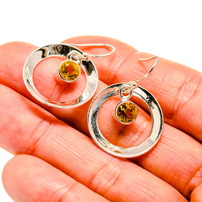 Sterling silver hoop earrings with round yellow faceted citrine, close-up on finger.