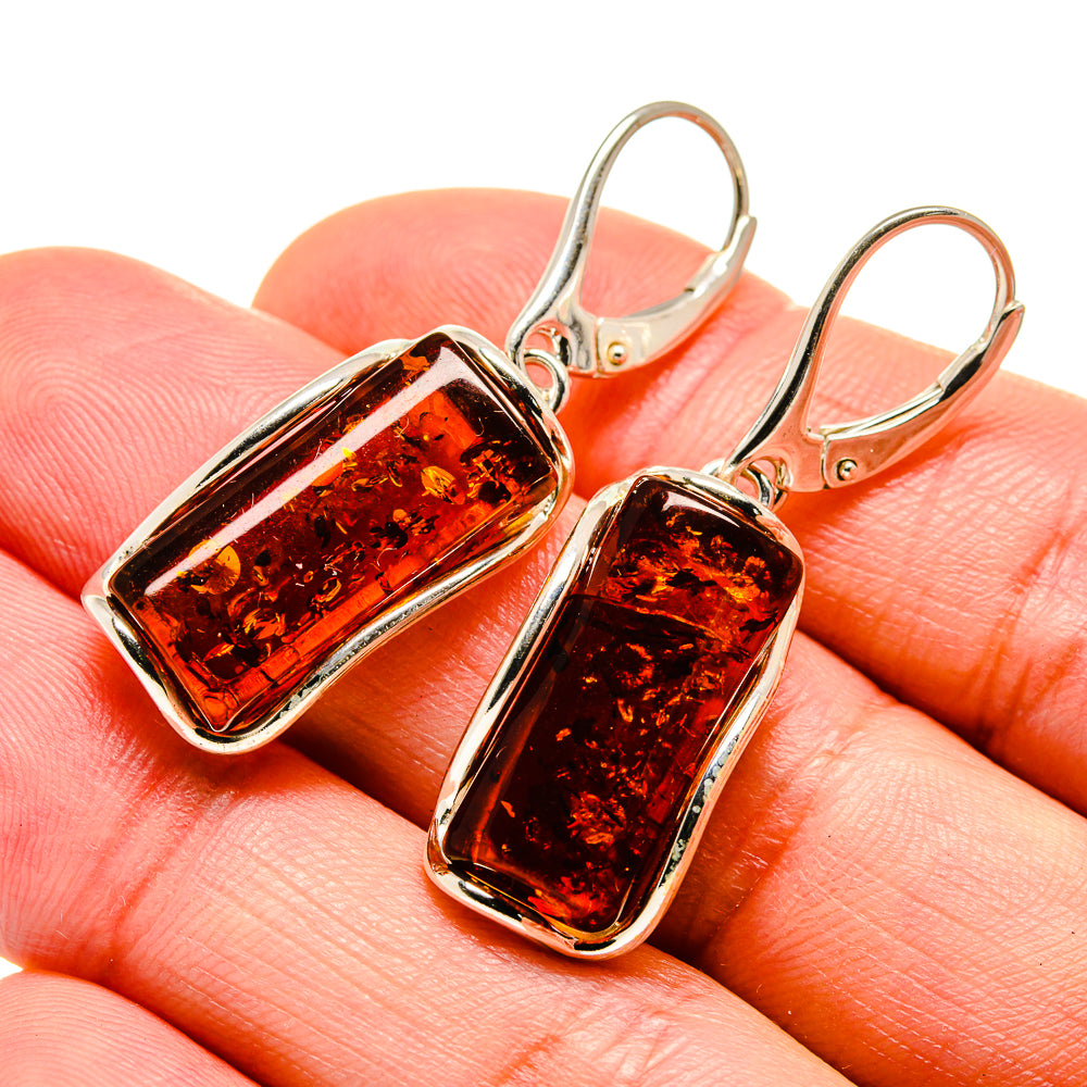 Rectangular amber drop earrings with silver frames and lever-back hooks on hand