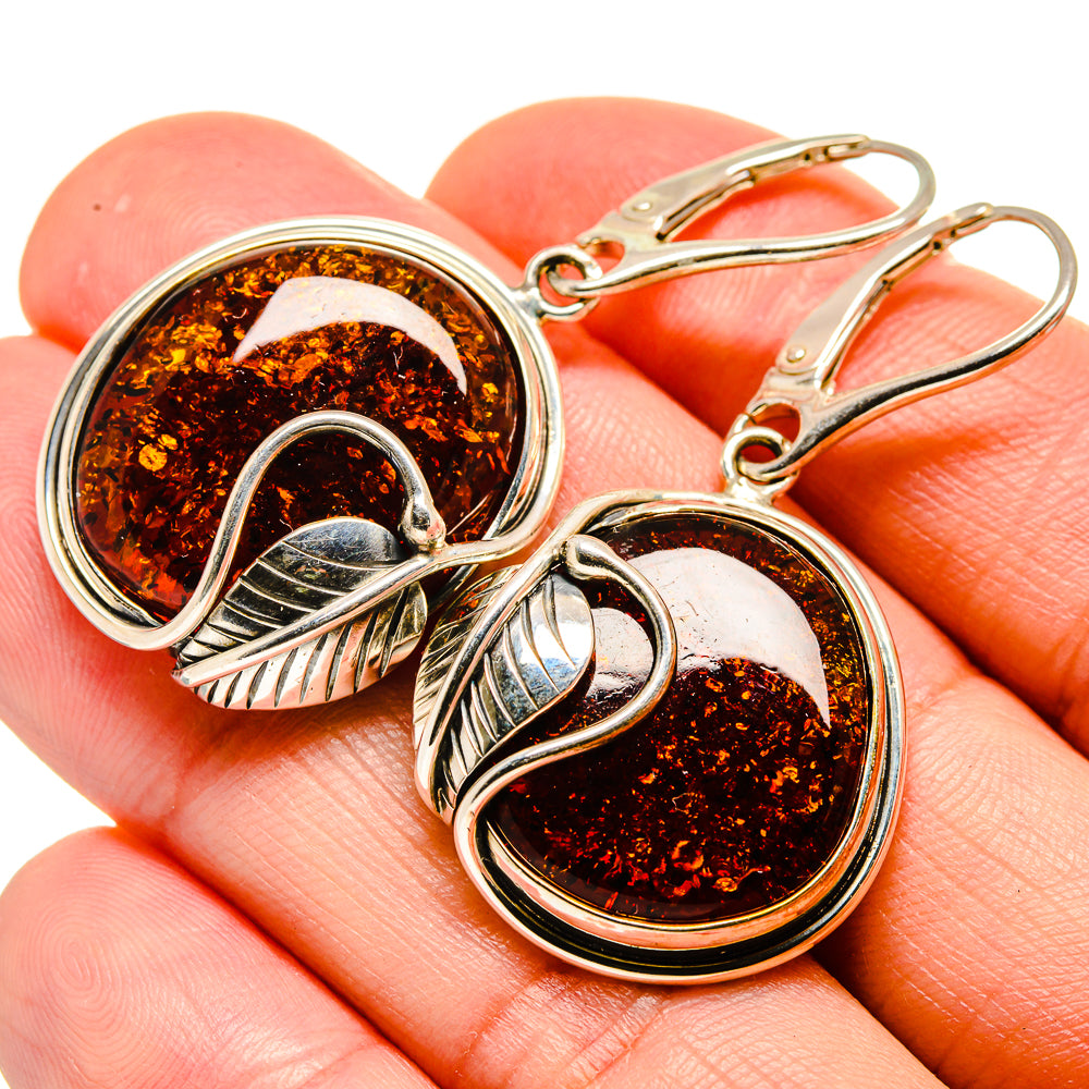 Amber cabochon hoop earrings with silver bezel and leaf-like accents, close-up on hand