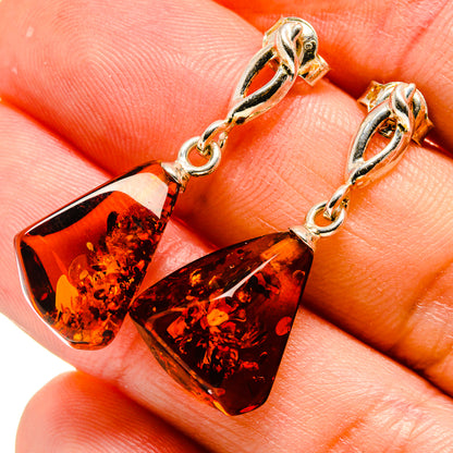 Close-up of amber teardrop earrings with silver-tone tops, chain links, and dangling drops