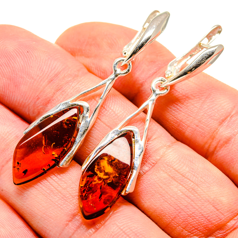Sterling silver drop earrings with amber teardrop stones, on finger close-up