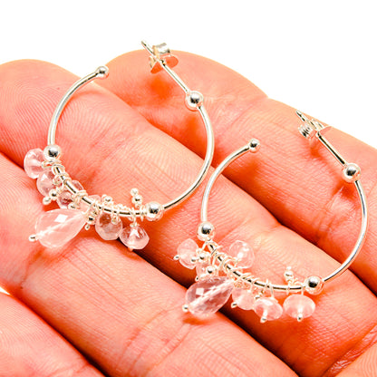 Closeup of silver hoop earrings with pink gemstone drop fringe