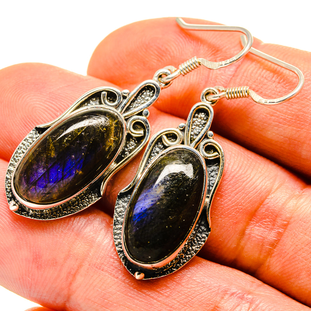 Oval labradorite earrings on hand, gold-tone hooked drops with iridescent yellow-blue stone