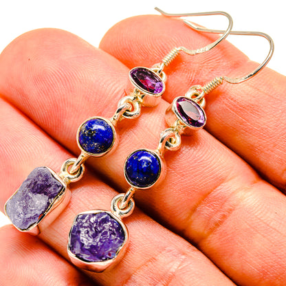 Gold-tone dangle earrings close-up with purple oval, blue round, and purple rough stones