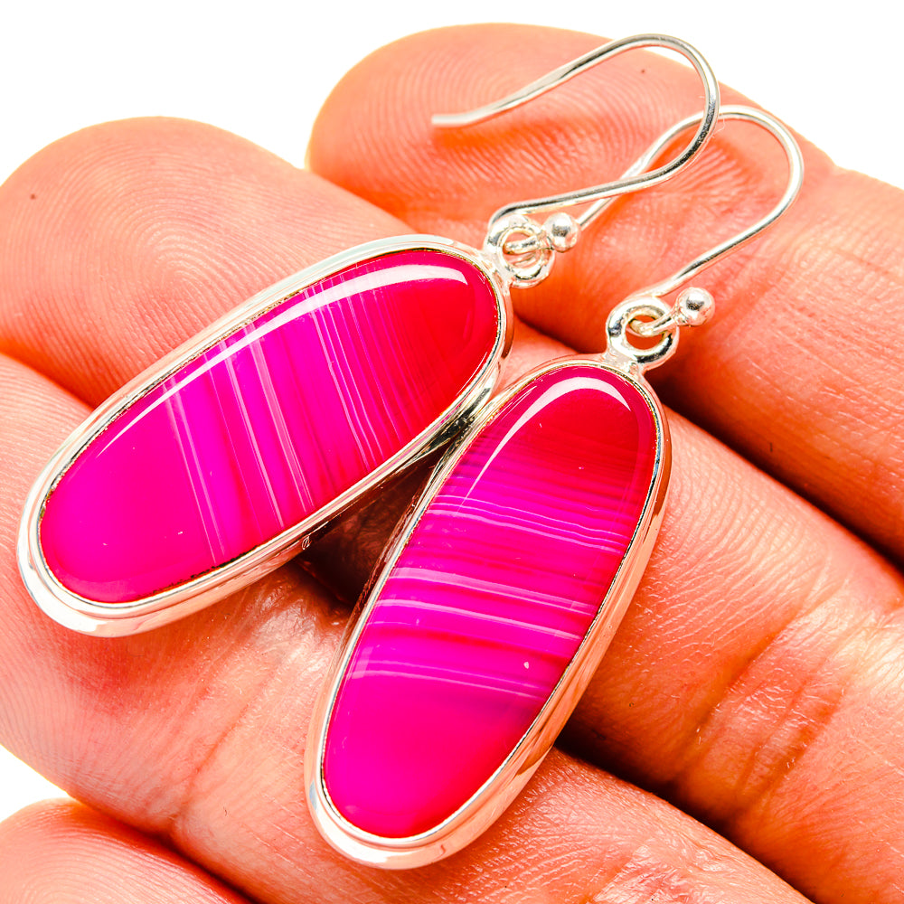 Pink agate teardrop earrings with silver hooks and bezel, close-up on finger