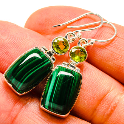 Green drop earrings with round peridot-colored stones and silver hooks, close-up on hand