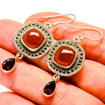 Gold-tone round earrings with red stone centers, ornate bezel, and red teardrop dangles