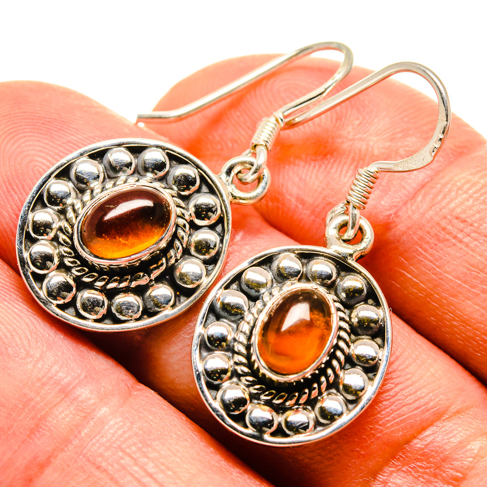 Close-up of round carnelian earrings: 925 silver hooks, beaded halo, amber oval cabochon.