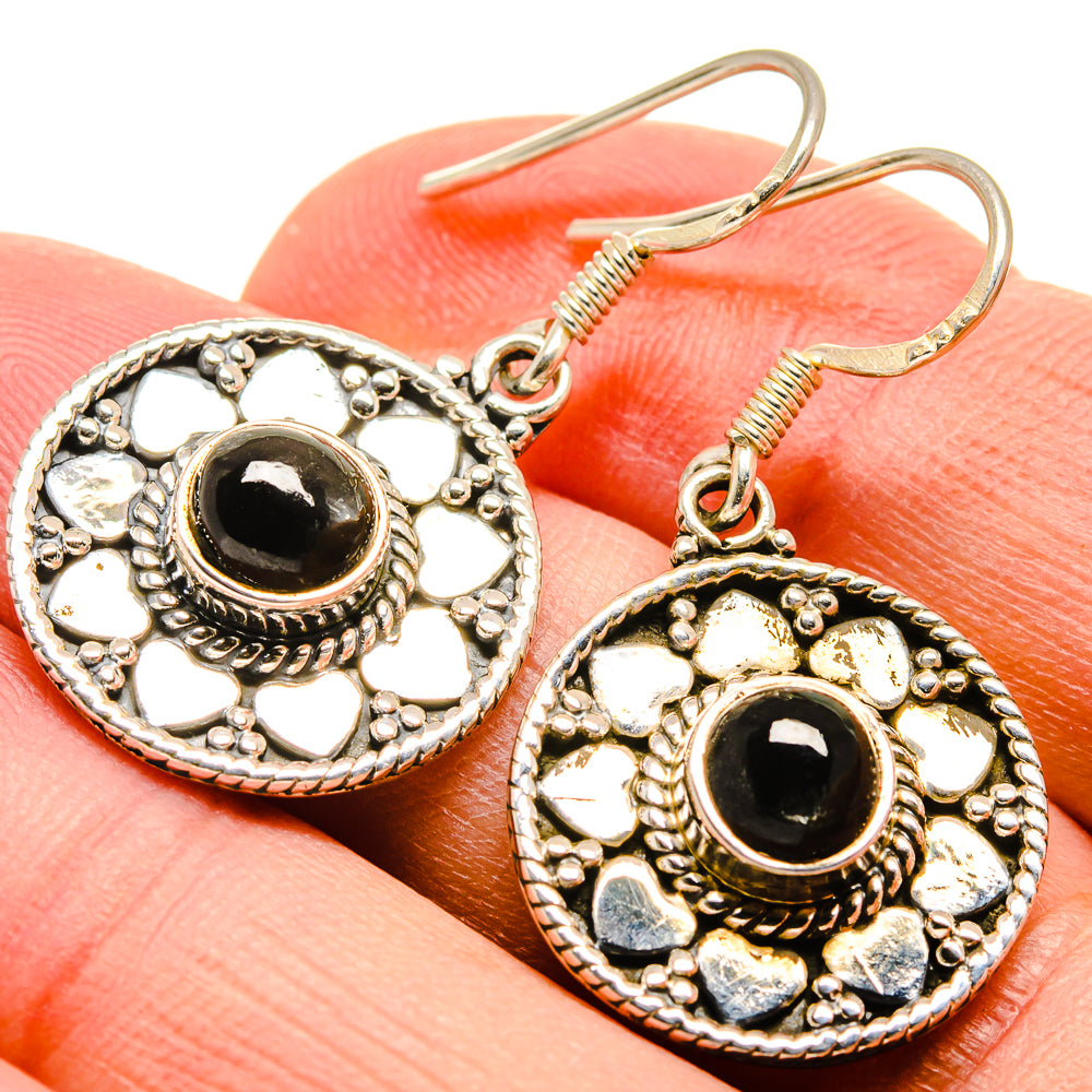 Closeup of round black onyx earrings with engraved silver-tone filigree and dangle hooks