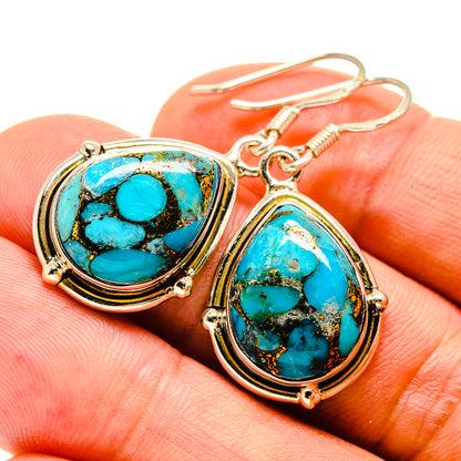 Turquoise oval cabochon earrings with gold-tone bezel and sterling silver hook, close-up.