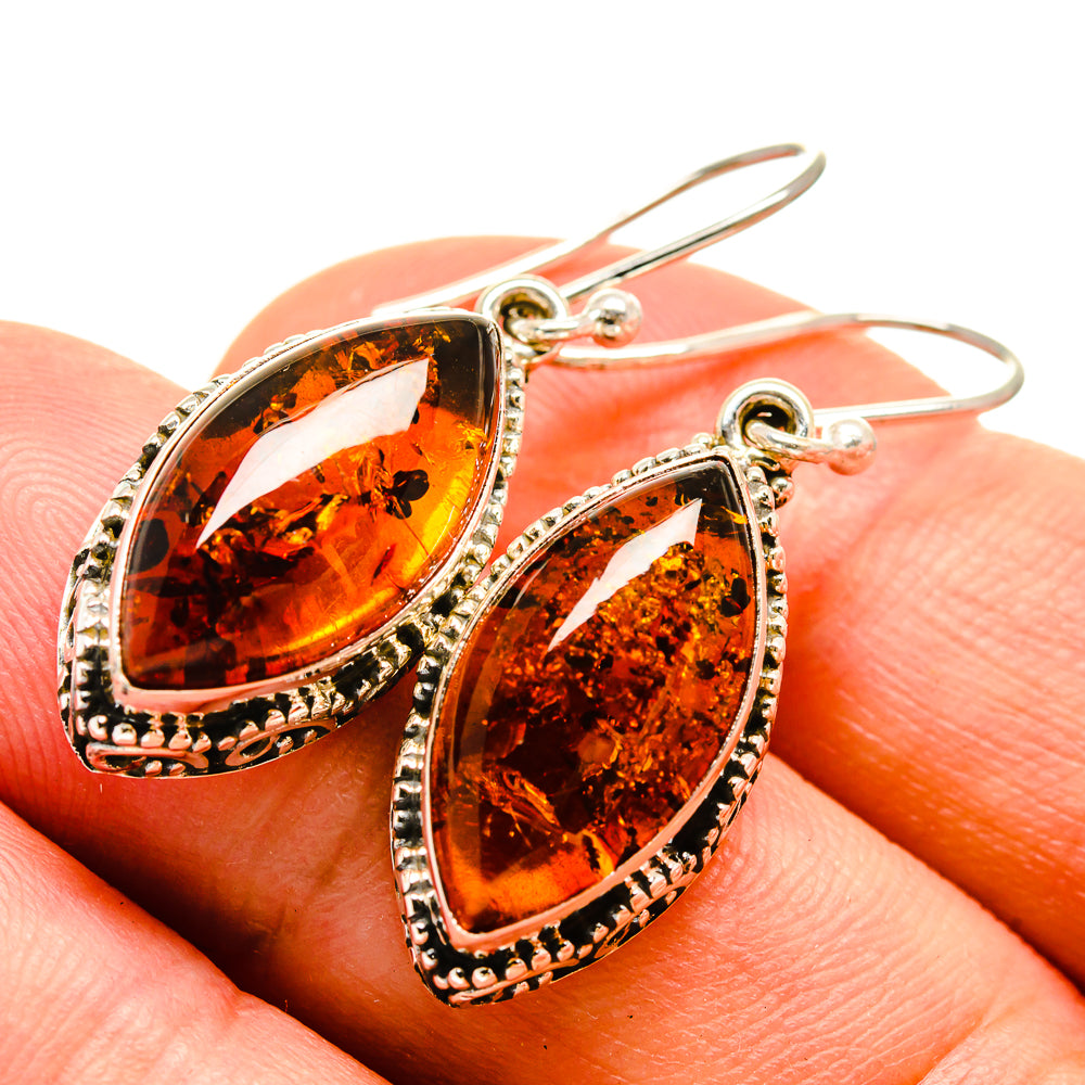 Baltic amber earrings close-up, oval amber cabochon with dark inclusions and silver hooks