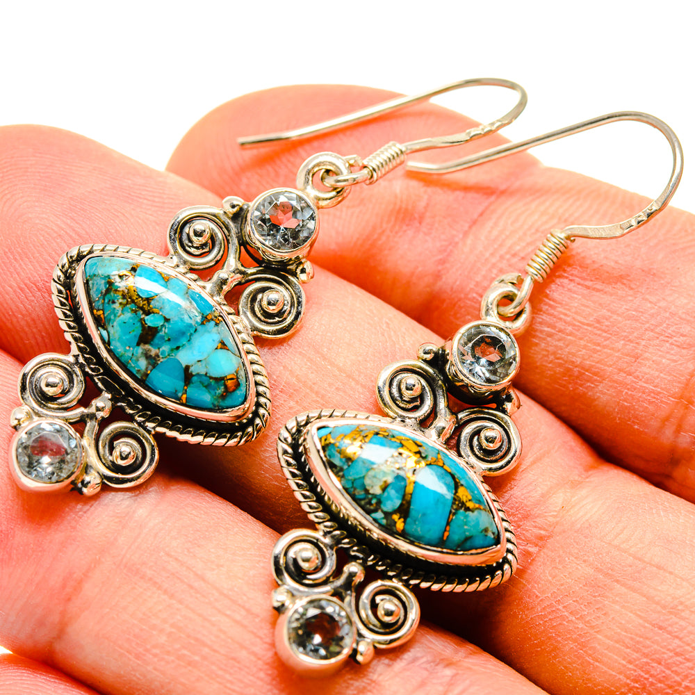 Gold-tone turquoise oval earrings with clear round stones, close-up on finger