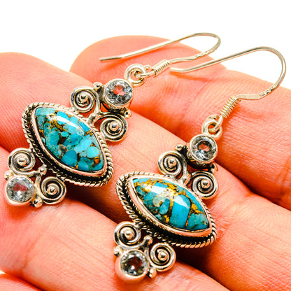 Gold-tone turquoise oval earrings with clear round stones, close-up on finger