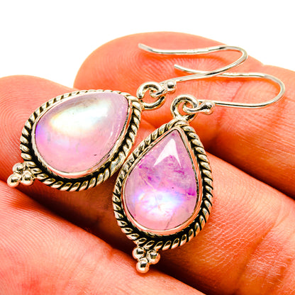 Close-up teardrop moonstone earrings with pink iridescent stones and ornate gold-tone hooks