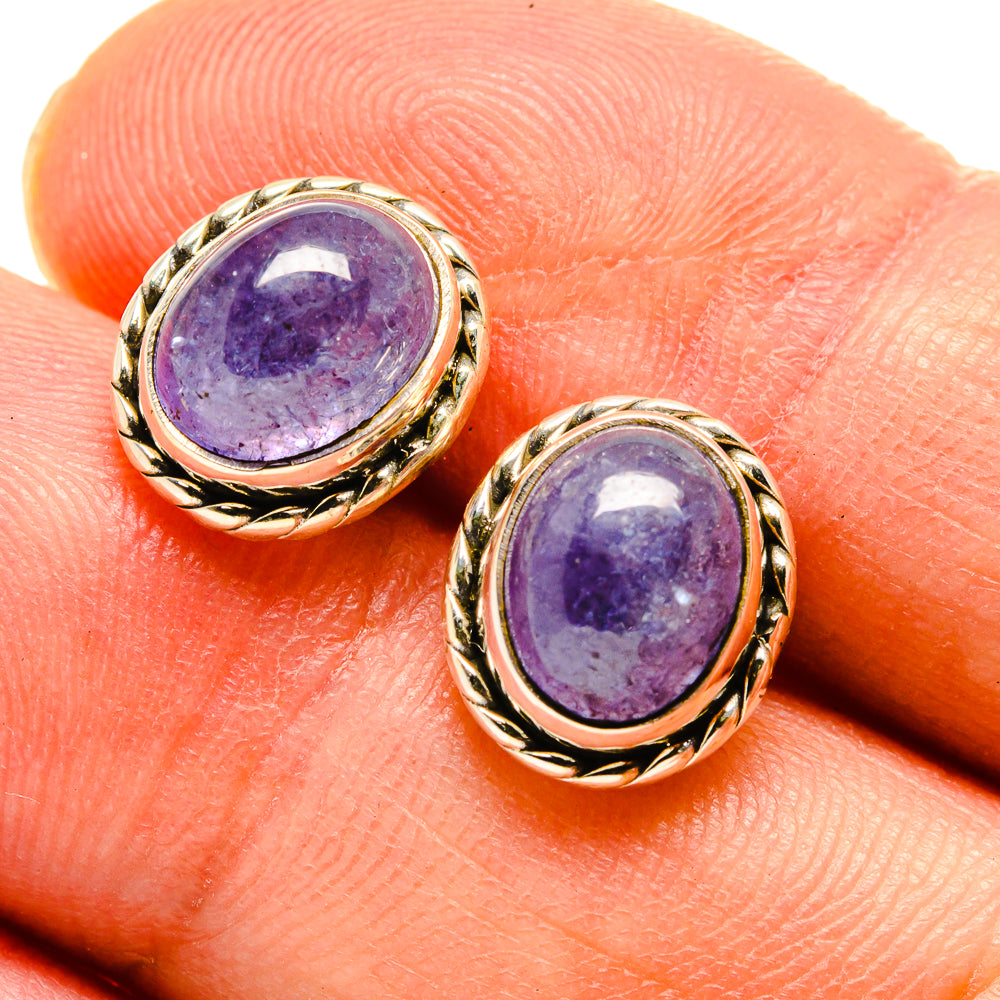 Oval purple gemstone stud earrings on fingertip, gold-tone bezel with rope detail