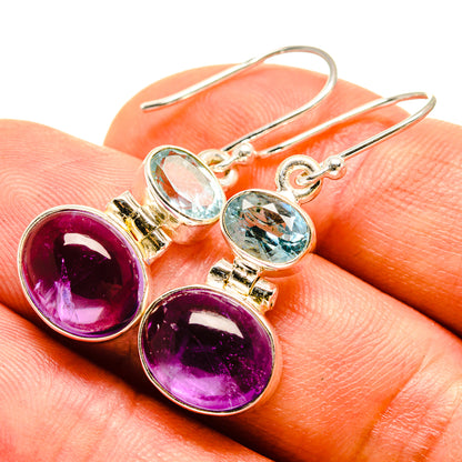 Silver drop earrings with oval purple amethyst and blue topaz stones, close-up on hand