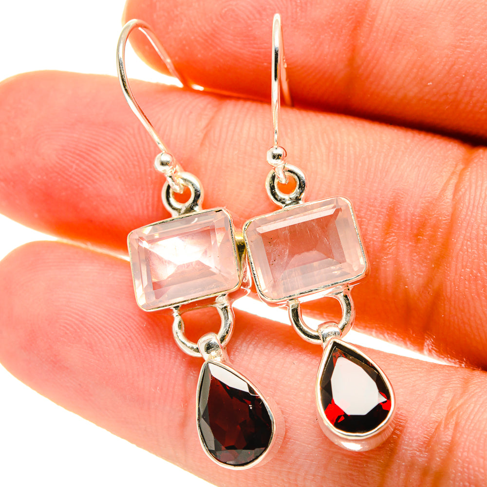 Close-up of silver earrings with square pink stones and red teardrop garnet drops