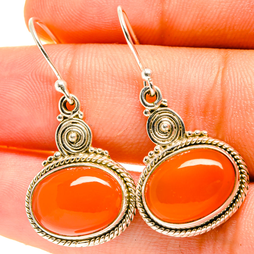 Orange carnelian cabochon earrings with hook, braided border, and round spiral top details