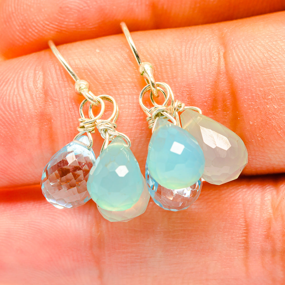 Close-up of metal-tone drop earrings with faceted clear and aqua teardrop stones
